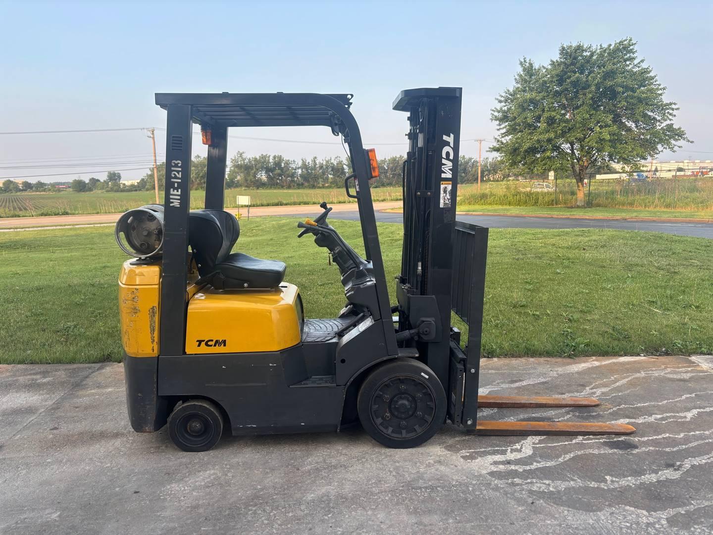 Yellow TCM forklift side view parked outdoors on grass edge