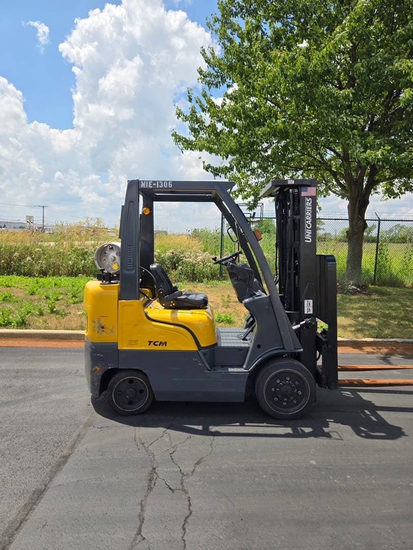 Yellow TCM forklift parked outdoors near tree